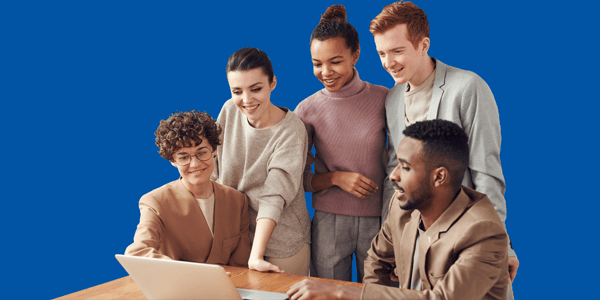 Photo of a group of people smiling and looking at a laptop on a table.