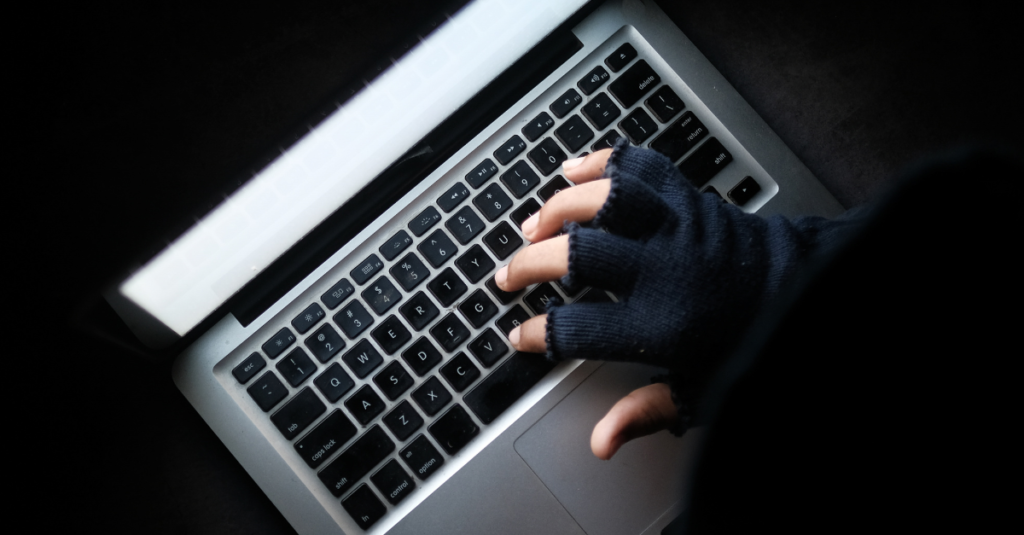 Hand wearing a fingerless glove typing on a laptop.