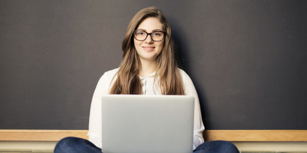 Person sitting behind a laptop wearing glasses and smiling.