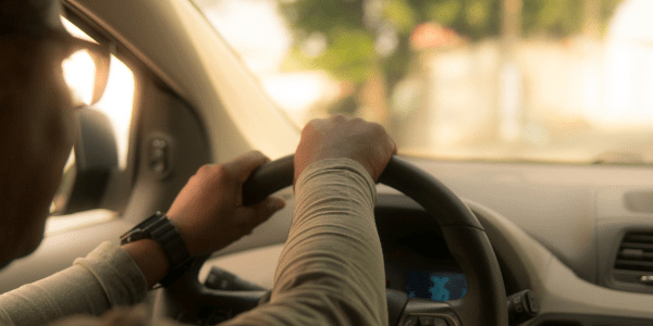 A person driving in a car with hands on the wheel.