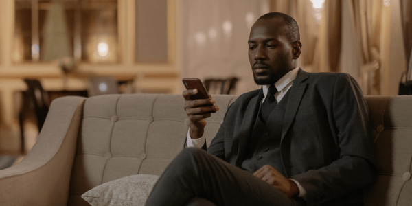 Person dressed in a suit, sitting on a sofa looking at and holding a cell phone.