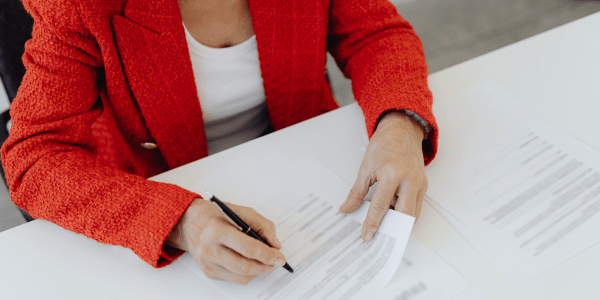 Person wearing a suit and holding a pen, writing on printed documents.