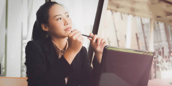 Person sitting and holding a pen with a laptop on the desk.